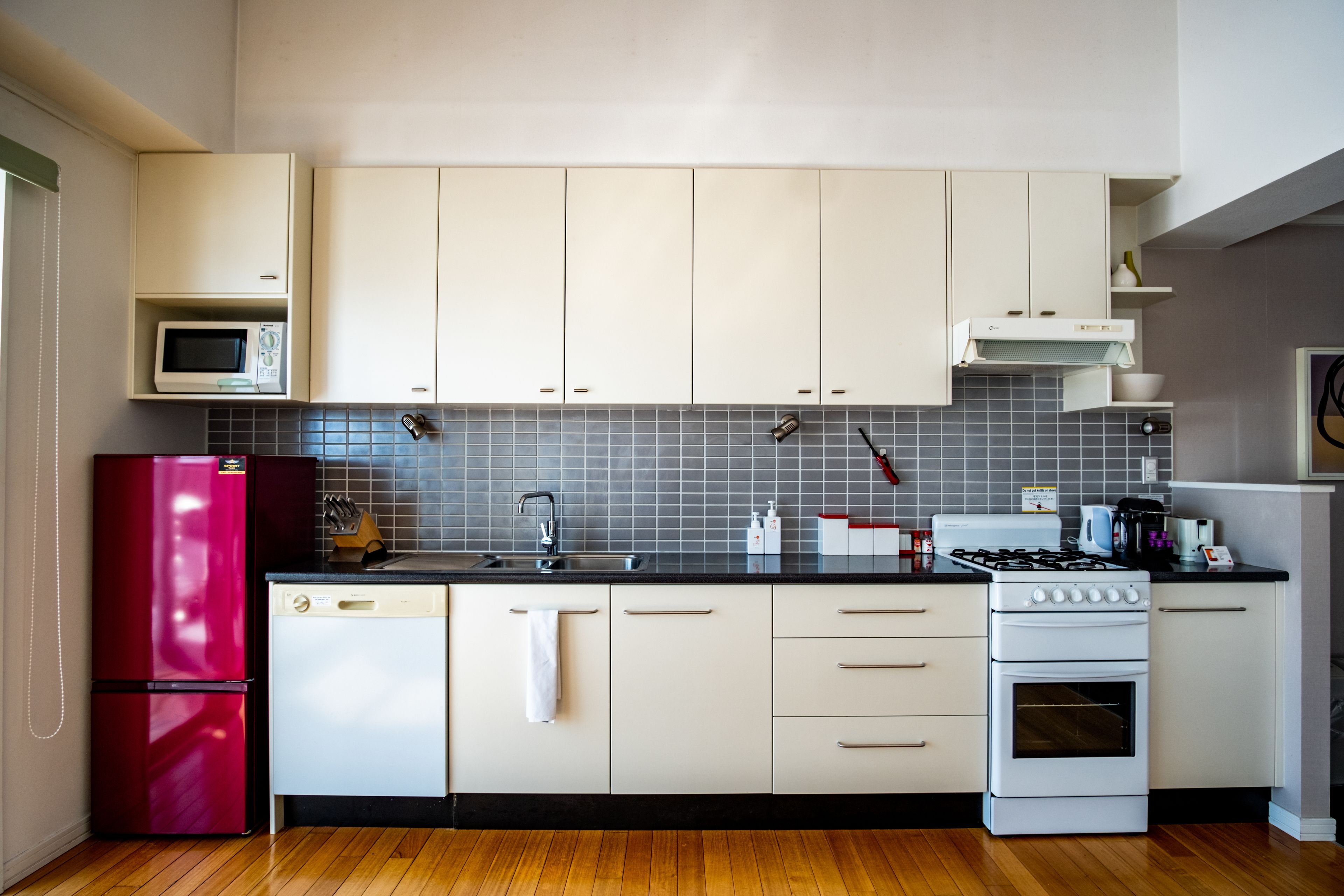 A kitchen with white cabinets, a red refrigerator, a microwave, a sink, a stove, and a dishwasher.