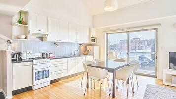 A modern kitchen with white cabinets, a dining table with chairs, and a large window offering a city view.