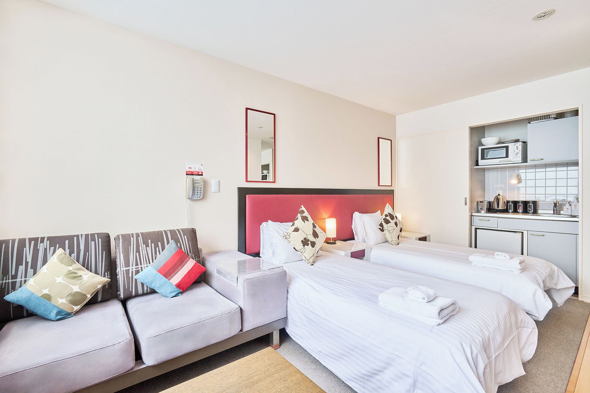 A hotel room with two beds, a sofa, a kitchenette, and a mirror.