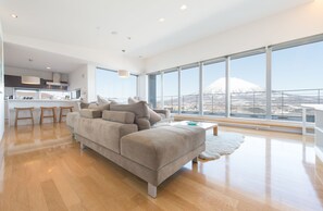 Un salon moderne avec un grand canapé gris, un plancher en bois et une vue sur une montagne, visible à travers de grandes fenêtres.