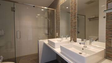A modern bathroom with two sinks, a glass shower enclosure, and a toilet.