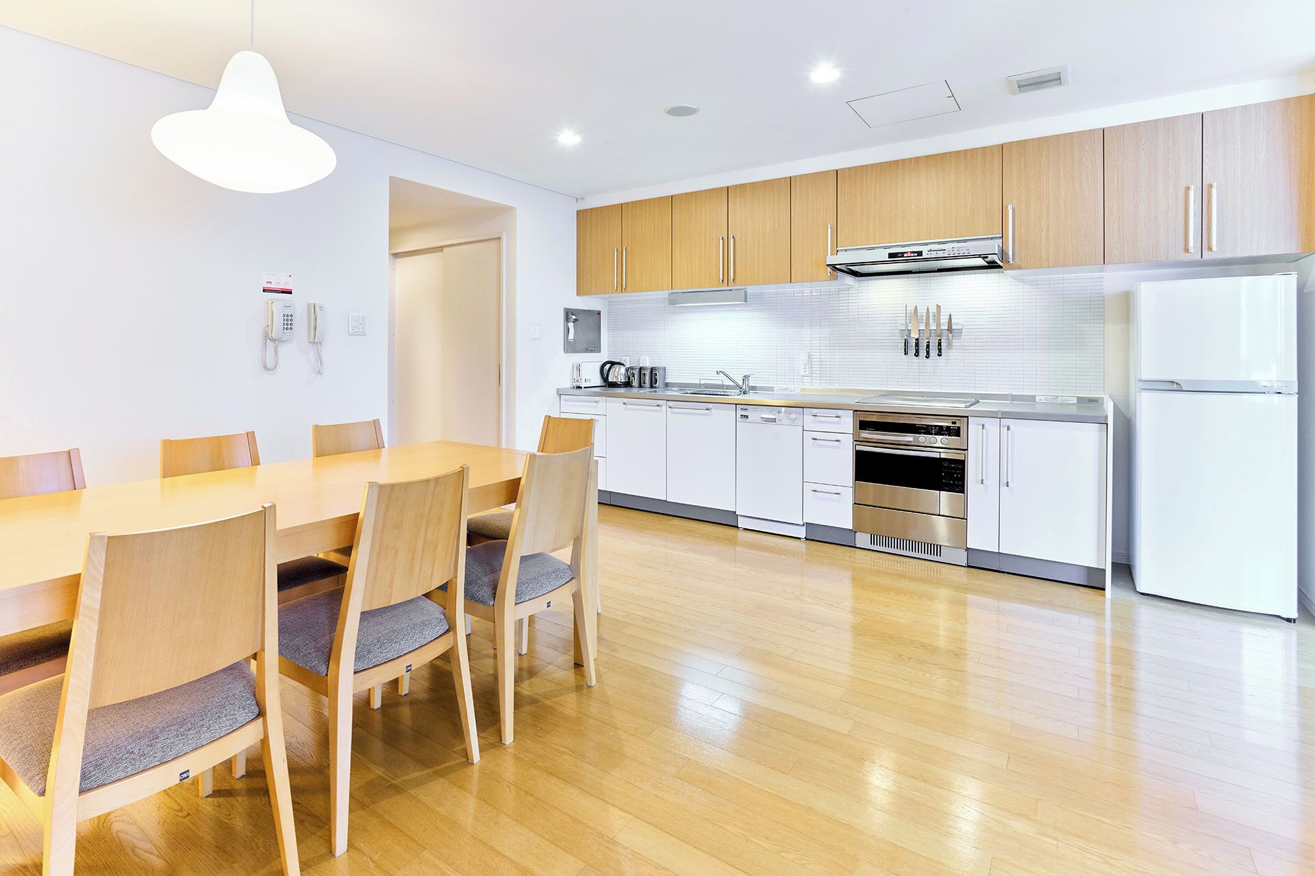 Una cocina moderna con armarios de madera, un refrigerador de acero inoxidable y un comedor con mesa y sillas de madera.