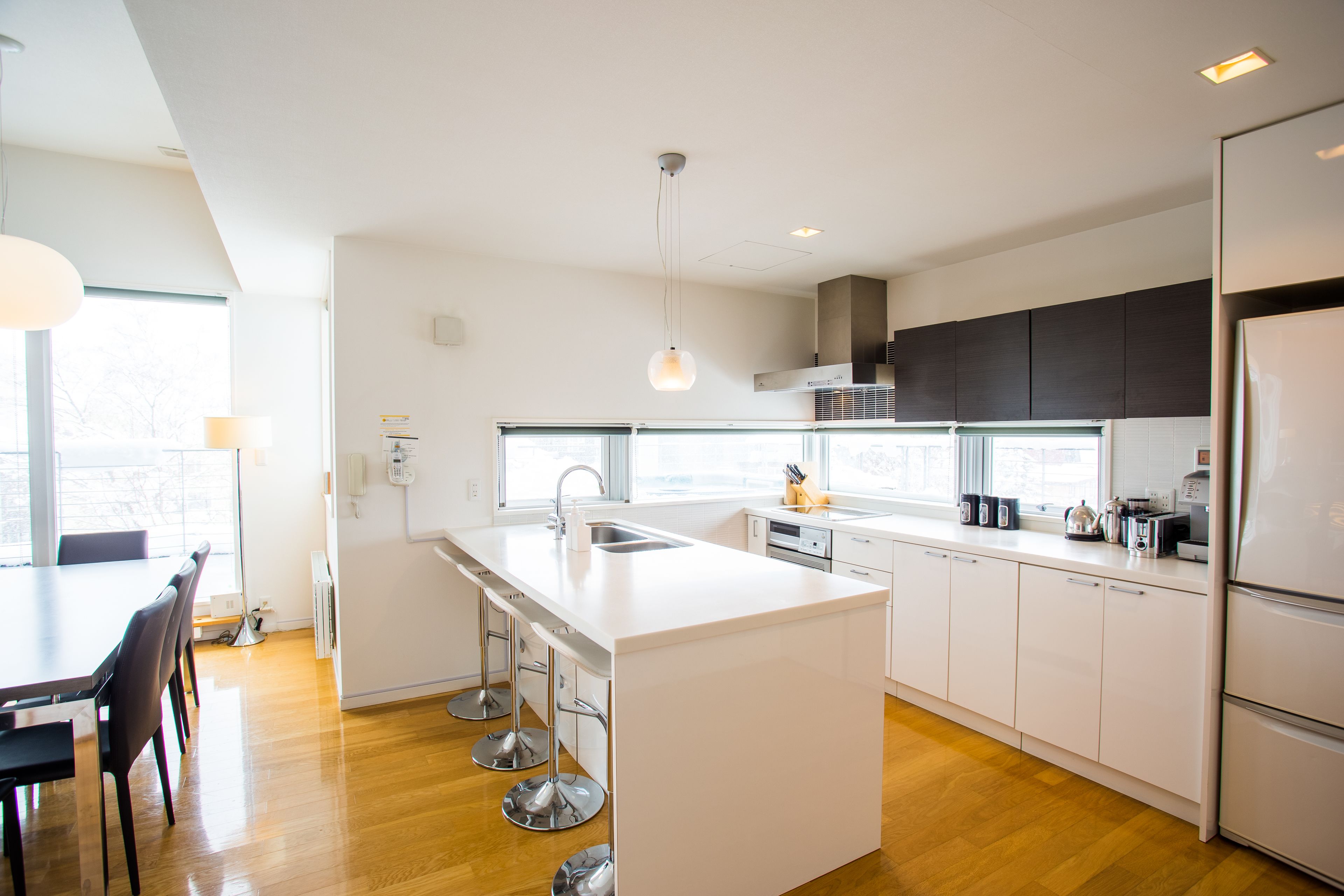 A modern kitchen with white cabinetry, a central island with bar stools, a built-in oven, and a large window providing natural light.