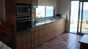 A kitchen with a microwave, oven, and granite countertop. There is a window with a view of the ocean. - WAVEBREAKER Scotts Head (Scotts Head)