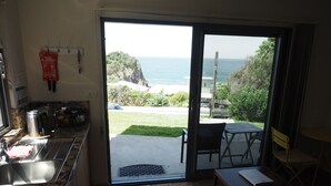 A kitchen with a sink, stove, and a view of the ocean through a sliding glass door. - WAVEBREAKER Scotts Head (Scotts Head)