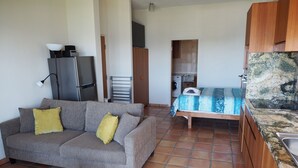 A compact living space with a sofa, a bed, a kitchenette, and a washing machine. - WAVEBREAKER Scotts Head (Scotts Head)