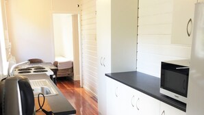 A compact kitchen with white cabinets, a black countertop, and a microwave. - The Little Cottage 3 minutes walk to beach. Beds for 5. (Henderson Bay)