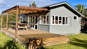 A small, single-story house with a covered patio and a wooden deck. - The Little Cottage 3 minutes walk to beach. Beds for 5. (Henderson Bay)