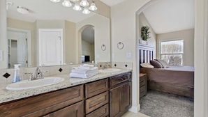 Une salle de bain avec deux lavabos, un grand miroir, des meubles en bois et une fenêtre avec des stores.