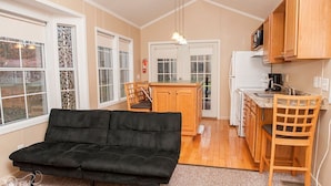 A compact living space with a sofa, wooden dining table, kitchen area, and large windows.