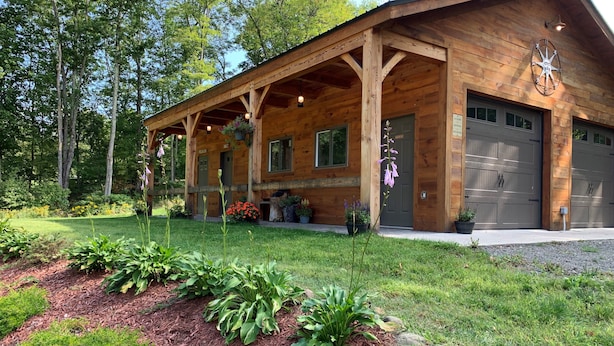 A wooden cabin with a covered porch, a garage, and a well-maintained garden with various plants and flowers.