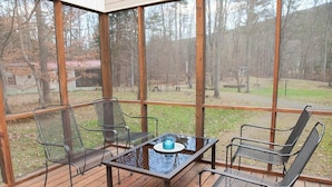 A covered outdoor area with a table and four chairs, surrounded by large windows.