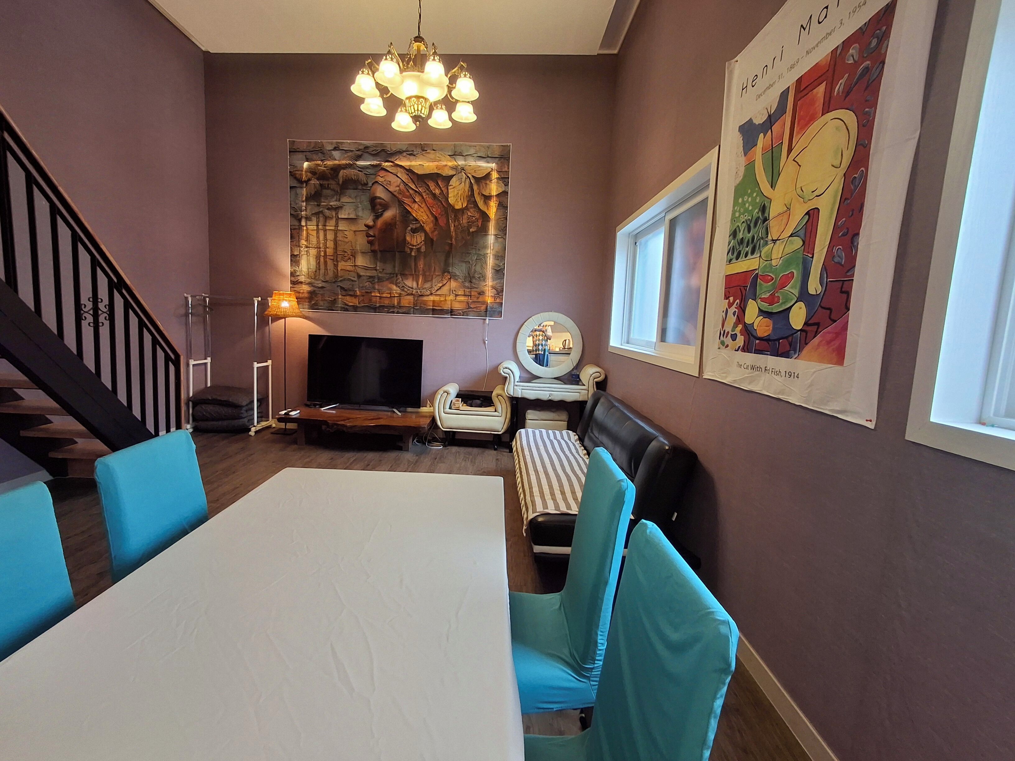 A dining area with a large table, blue chairs, a chandelier, a television, and artwork on the walls.
