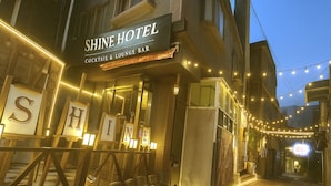 Shine-hotellin ulkopuoli, jossa on cocktailbaari ja oleskelutila, ja jossa on valaistut kirjaimet ja koristeelliset valonauhat.