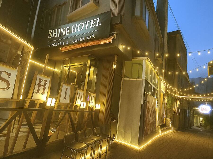 Exterior del hotel Shine, con bar de cócteles y bar lounge, con letras iluminadas y guirnaldas de luces.
