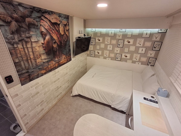Una habitación pequeña y moderna con una pared de ladrillo, un mural, una cama, un televisor y una pared de cuadros enmarcados.