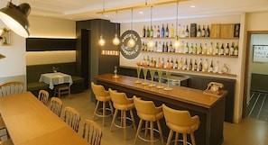 Un bar salón en el primer piso con barra, taburetes y una pared llena de botellas de vino.