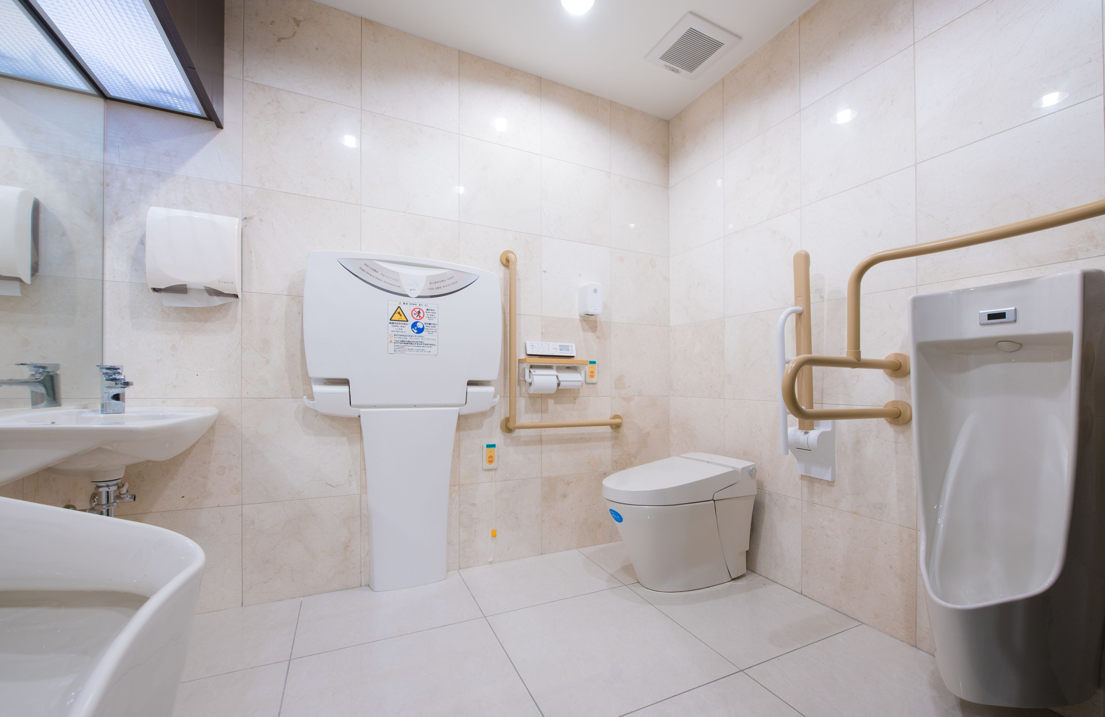 Un baño moderno con inodoro, orinal, lavamanos y secamanos.