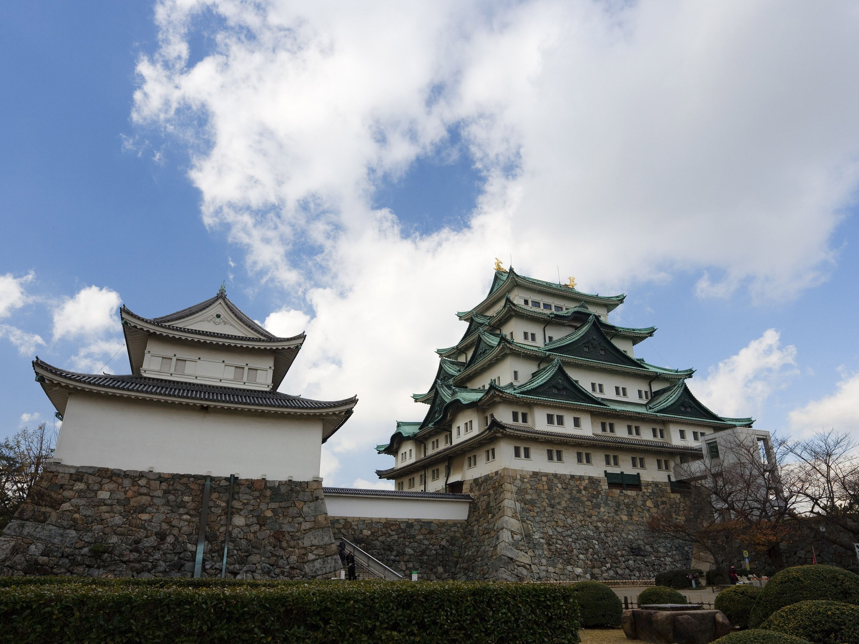 A traditional Japanese castle with multiple tiers and green roofs, surrounded by stone walls and well-maintained gardens.
