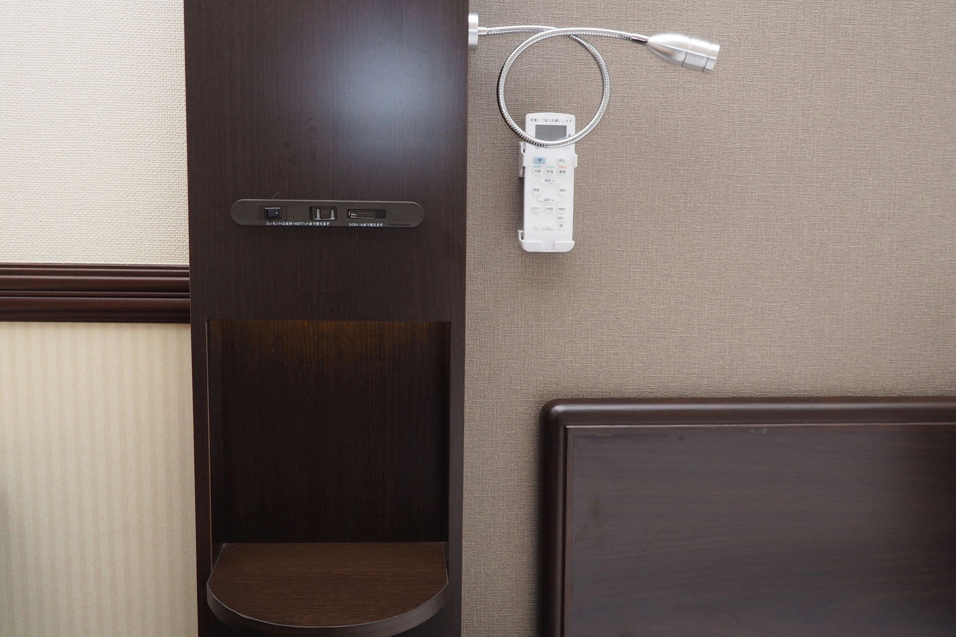 Una habitación de hotel con un armario de madera, un estante pequeño de madera, una cama y un enchufe de pared con una regleta.