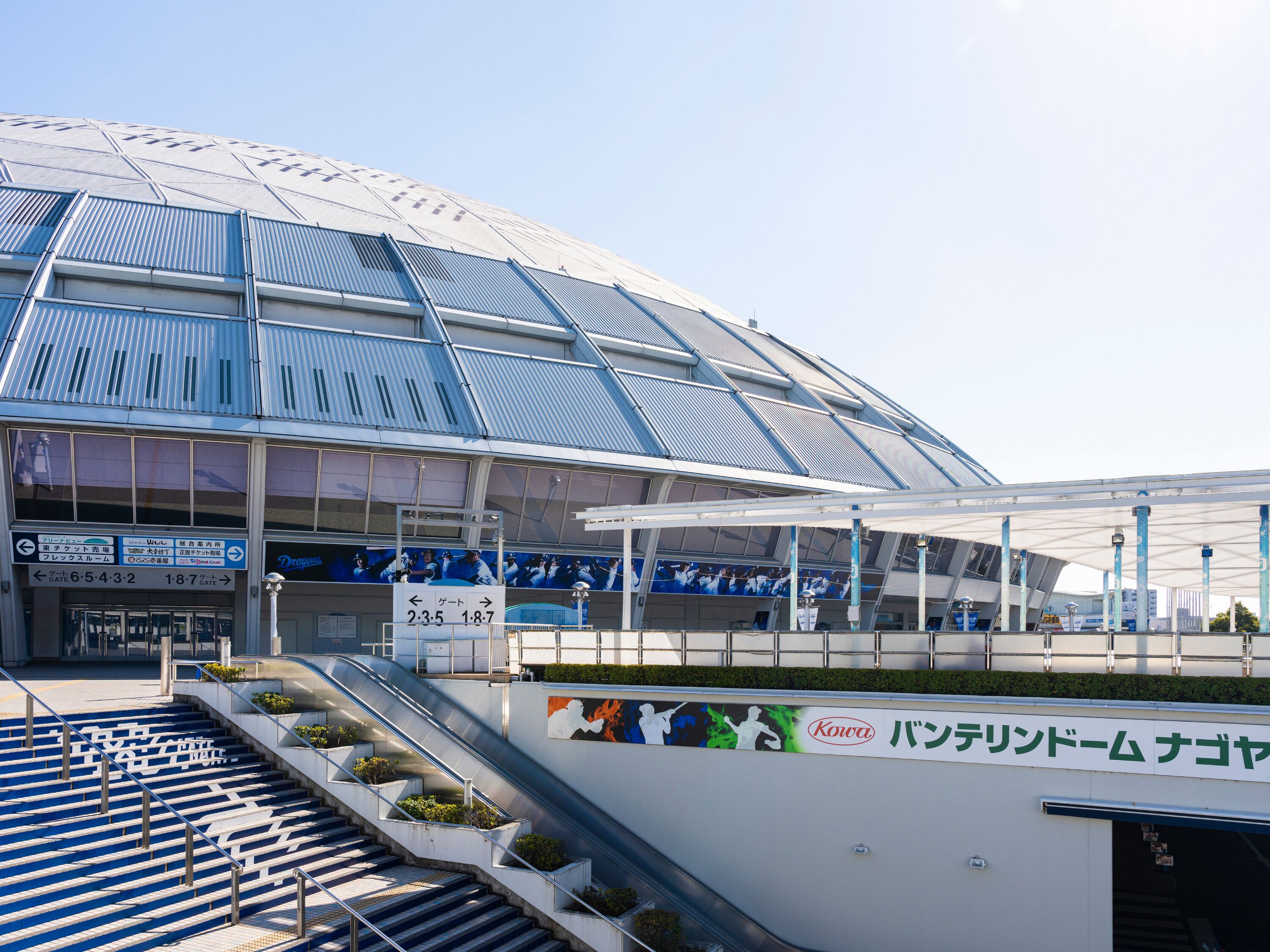 A stadium with a large seating area, an escalator leading to the entrance, and a sign with a time schedule.