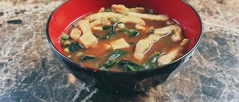Un bol de soupe contenant du tofu et des légumes verts, posé sur une surface en marbre.