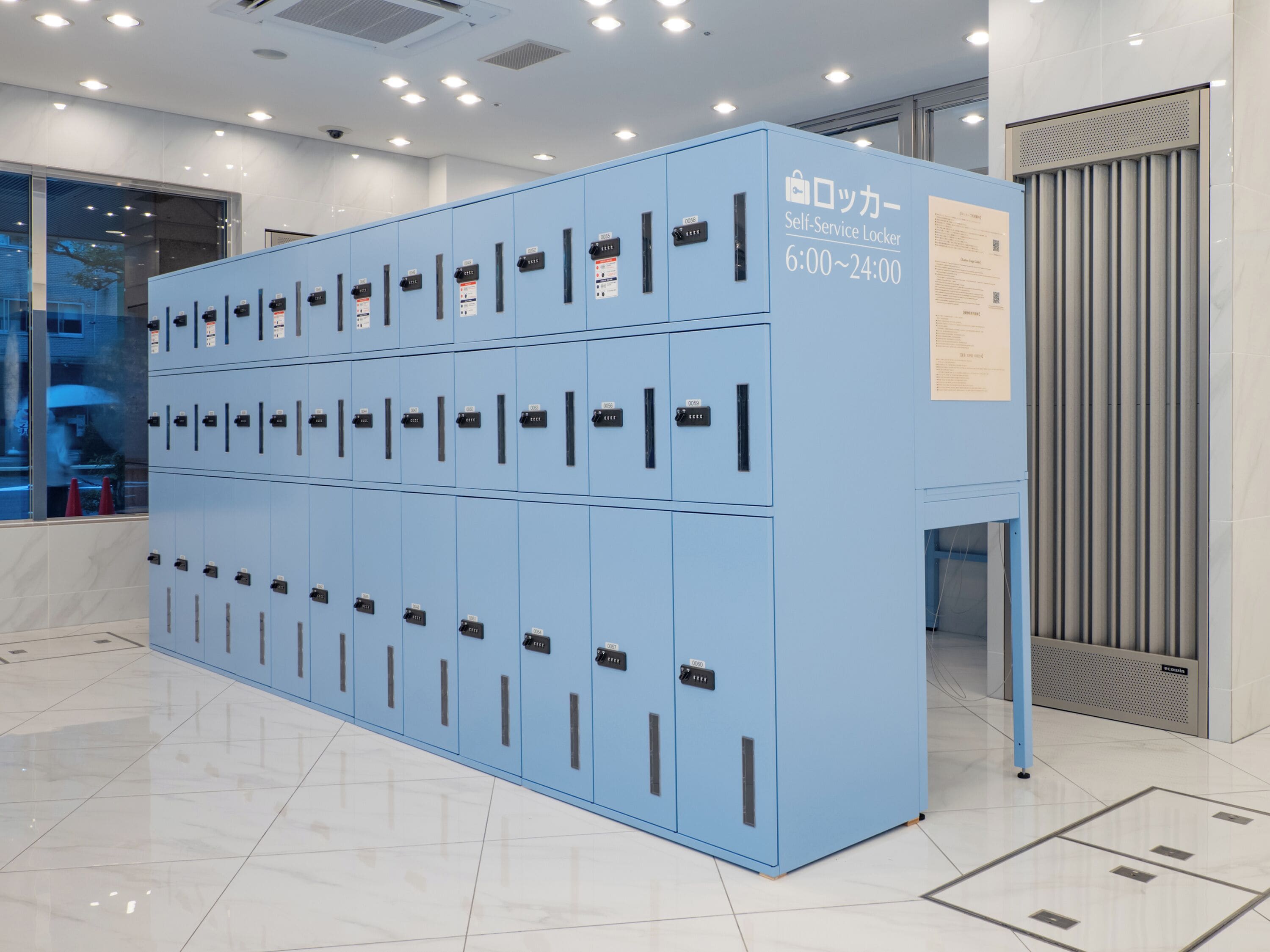 A row of blue self-service lockers with numbered compartments, a sign indicating operating hours, and a ventilation unit to the right.