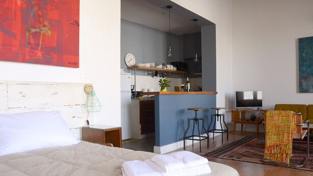 Hotellihuone, jossa on sänky, työpöytä, tuoli, televisio ja pieni keittiönurkkaus.