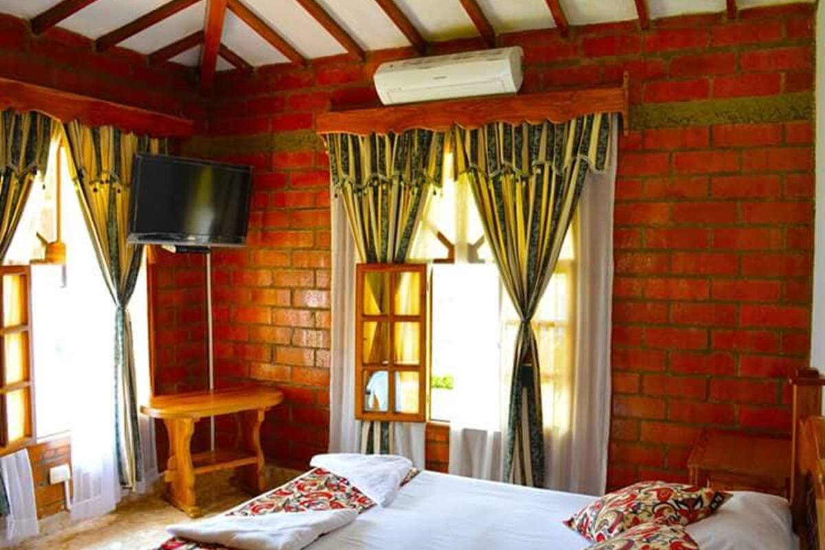 Ein Zimmer mit Backsteinwand, einem Bett mit gemusterten Kissen, einem Holztisch und einem an der Wand befestigten Fernseher.