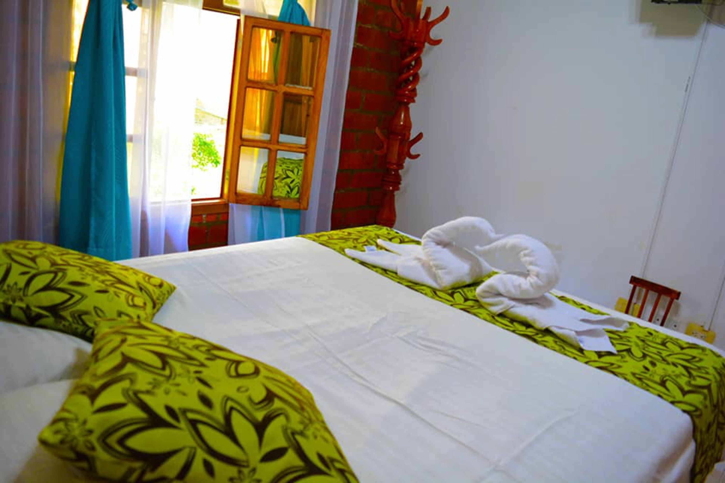 A bed with green and white bedding, a wooden window frame, and a red wall decoration.
