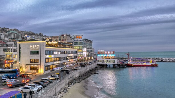 A coastal hotel with multiple floors, a prominent MIPO sign, and a ferry docked at the pier. - Mipo Oceanside Hotel (Busan)