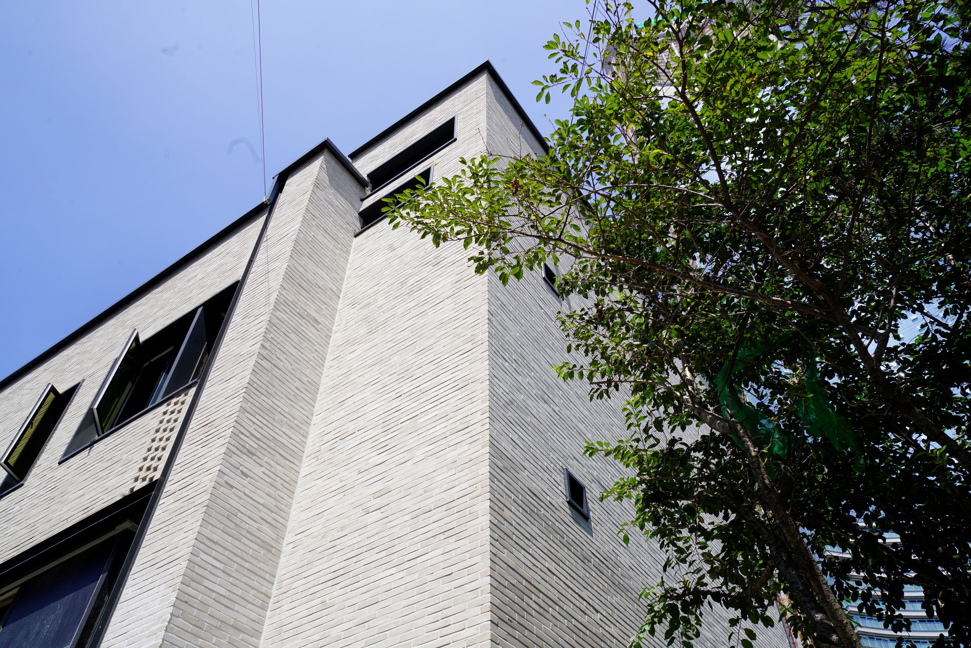 A modern building with a prominent corner, large windows, and a tree in the foreground.