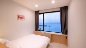 A bedroom with a large window, a bed, and a small wooden nightstand. - Mipo Oceanside Hotel (Busan)