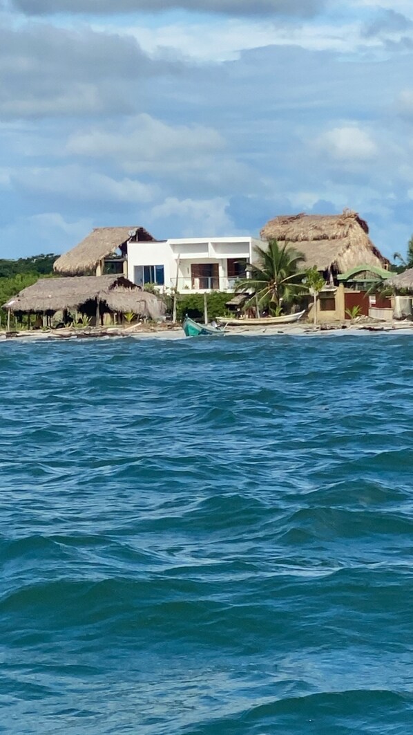 Une propriété située en bord de mer, comprenant une structure à toit de chaume, un bâtiment moderne et un bateau amarré près du rivage.