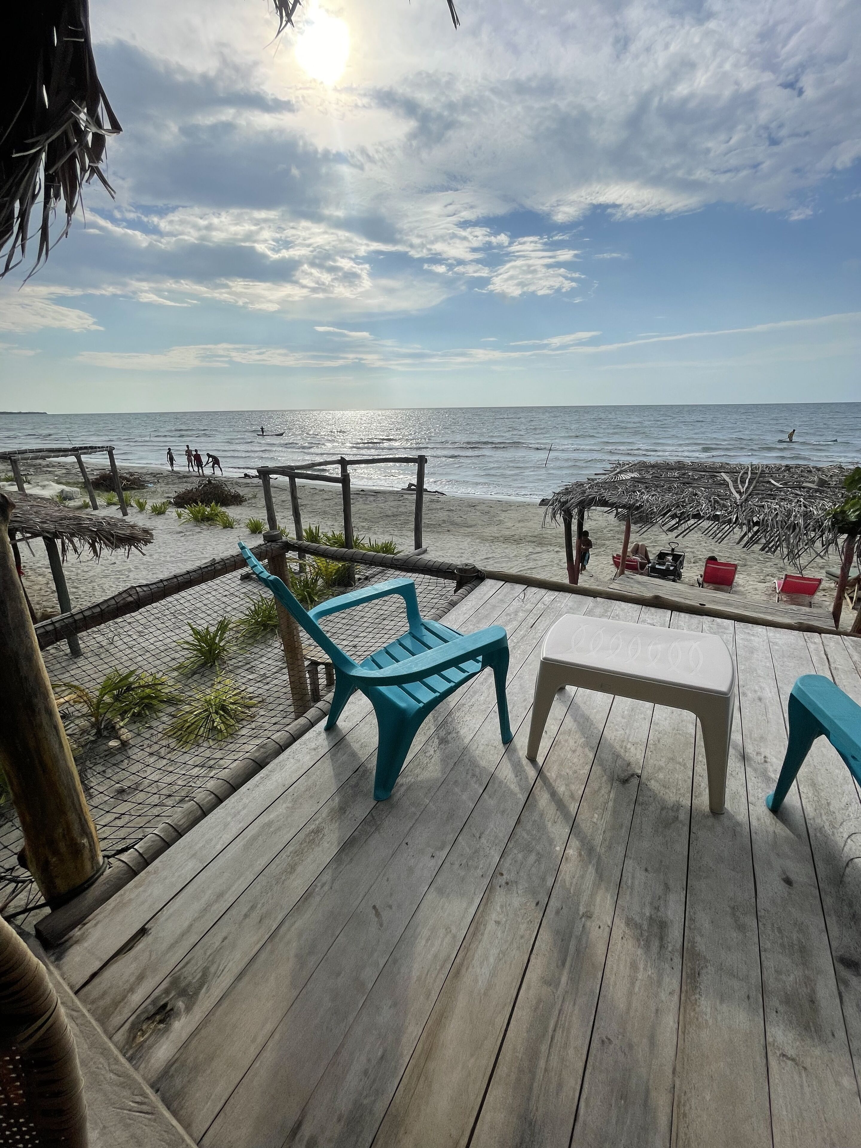 Terraza de madera con sillas y una mesa con vista a una playa y una estructura de techo de paja.
