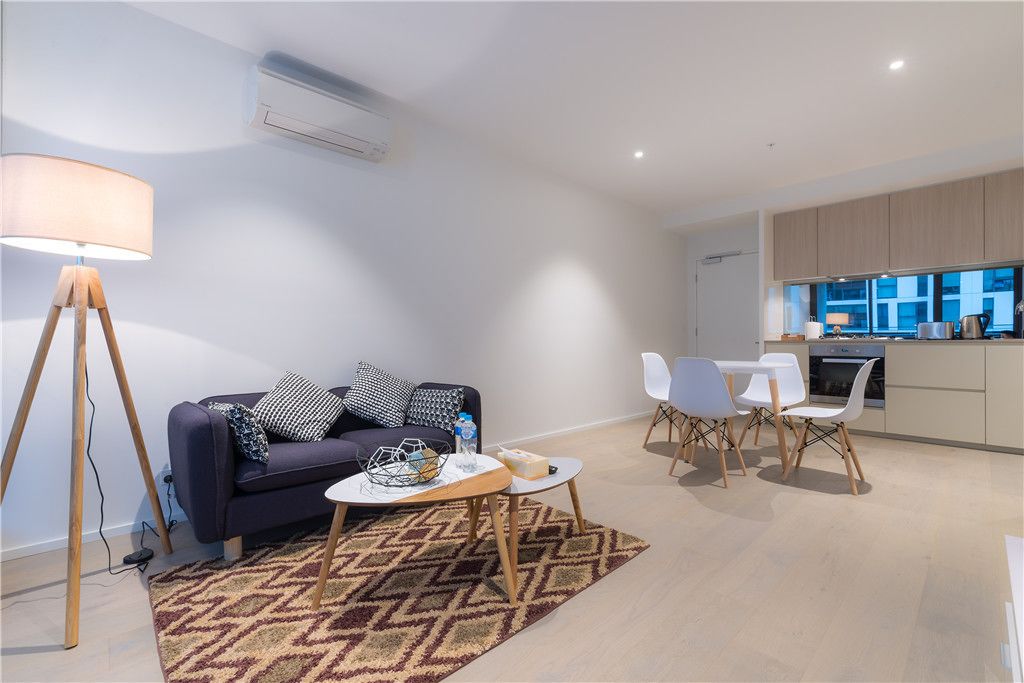 Una sala de estar moderna con sofá, mesa de centro y sillas. Hay una zona de cocina con armarios y una ventana.