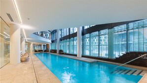 An indoor swimming pool with clear glass walls, a tiled floor, and a modern architectural design. - APC on Collins (Docklands)