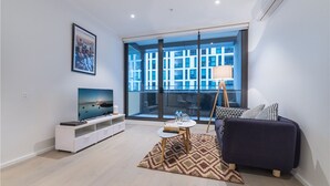 A modern living room with a large TV, a sofa, a coffee table, and a patterned rug. - APC on Collins (Docklands)