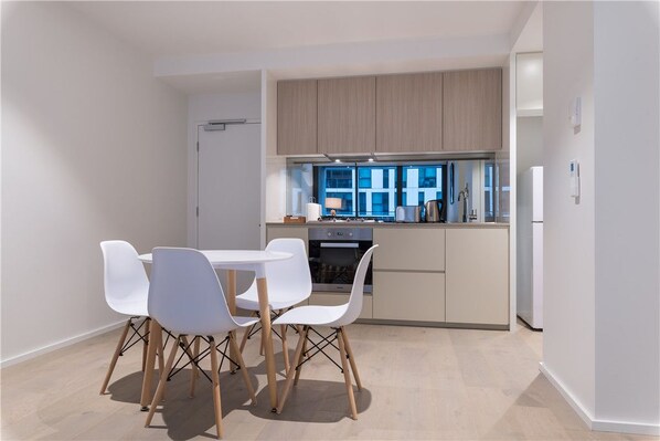 A modern kitchen with a dining area, featuring a white table and chairs, wooden cabinets, and a view of the city.