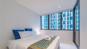 A modern hotel room with a large bed, a window with a city view, and a small bedside table. - APC on Collins (Docklands)