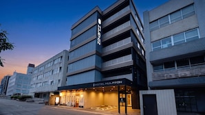 Ein modernes Hotelgebäude mit mehreren Etagen, einem markanten Eingang und blauem Himmel.
