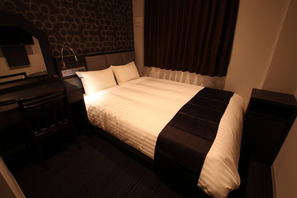 Ein Hotelzimmer mit einem großen Bett, einem Schreibtisch mit Lampe und einem Kopfteil mit geometrischem Muster.
