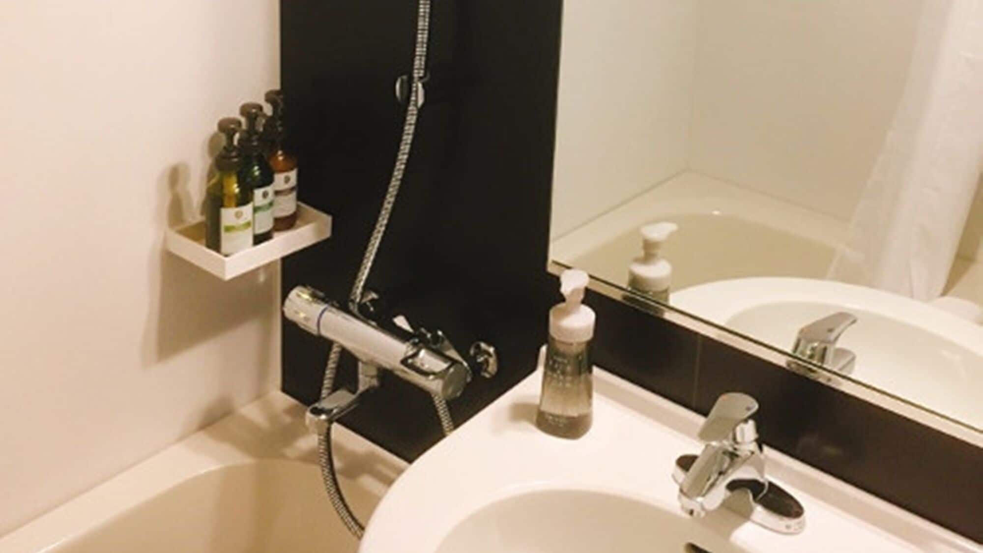 A bathroom with a white sink, a mirror, a shower, and a shelf with toiletries.