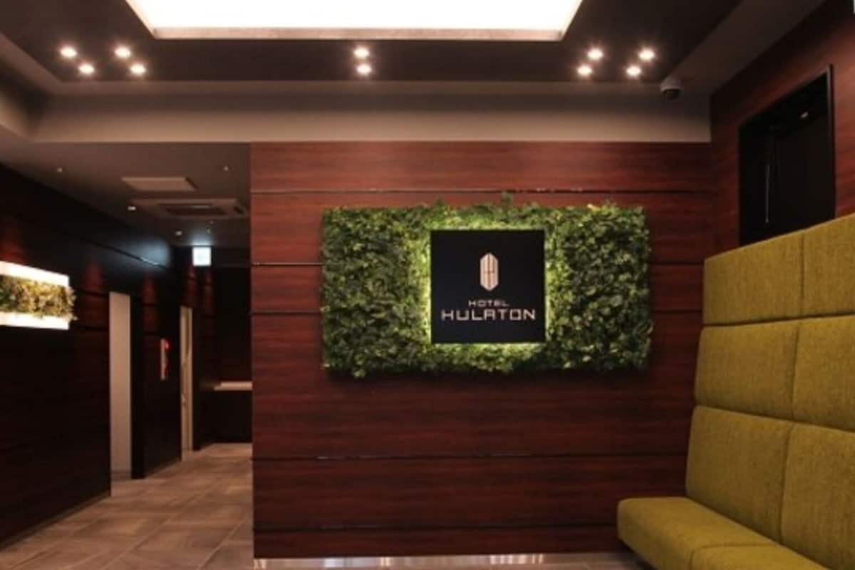 Una zona de recepción con un mostrador de madera, una pared verde con un logotipo y un sofá amarillo.