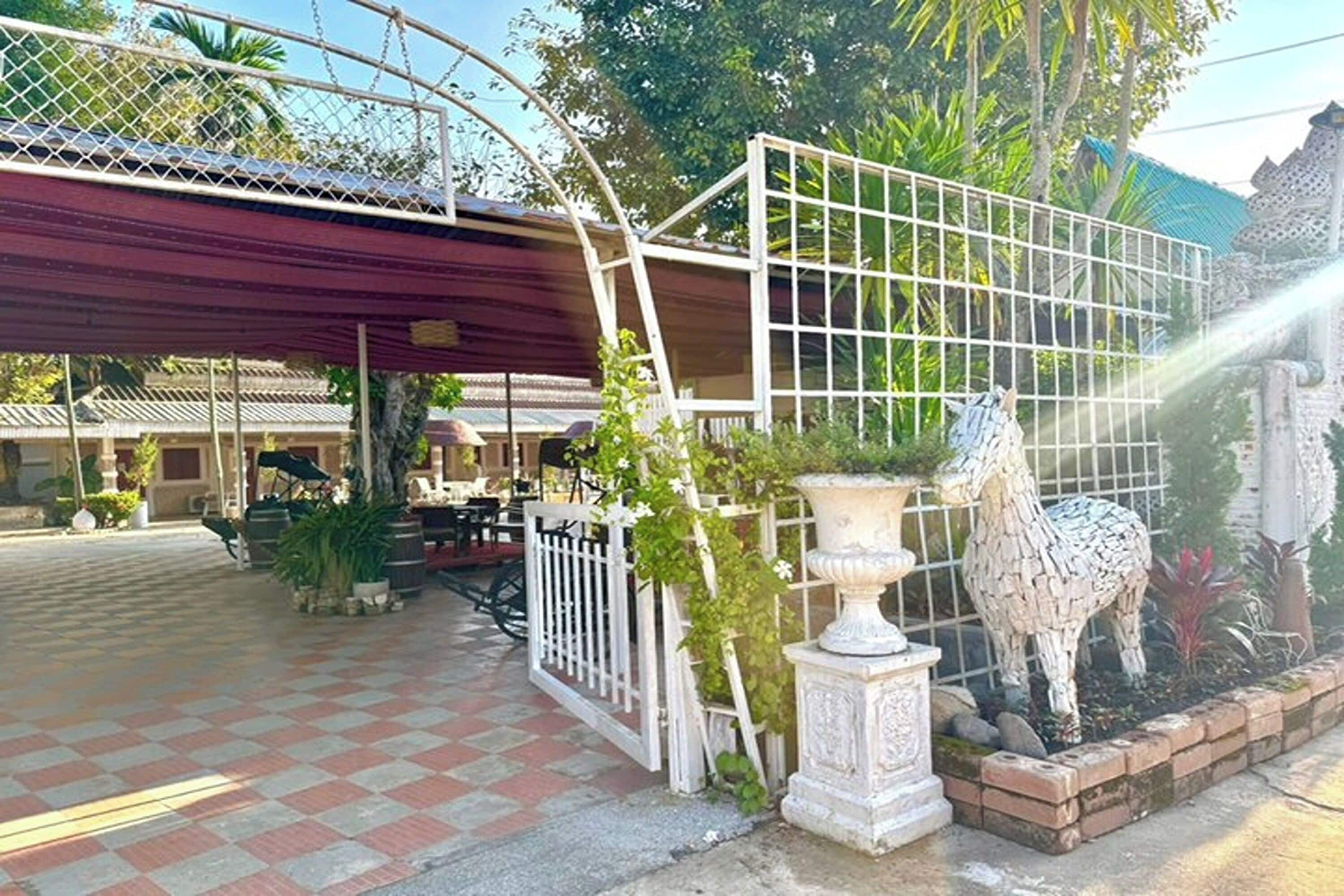 Ein Innenhof mit Schachbrettmuster-Boden, weißem Zaun, einer überdachten Sitzgruppe und einer dekorativen Pferdestatue.