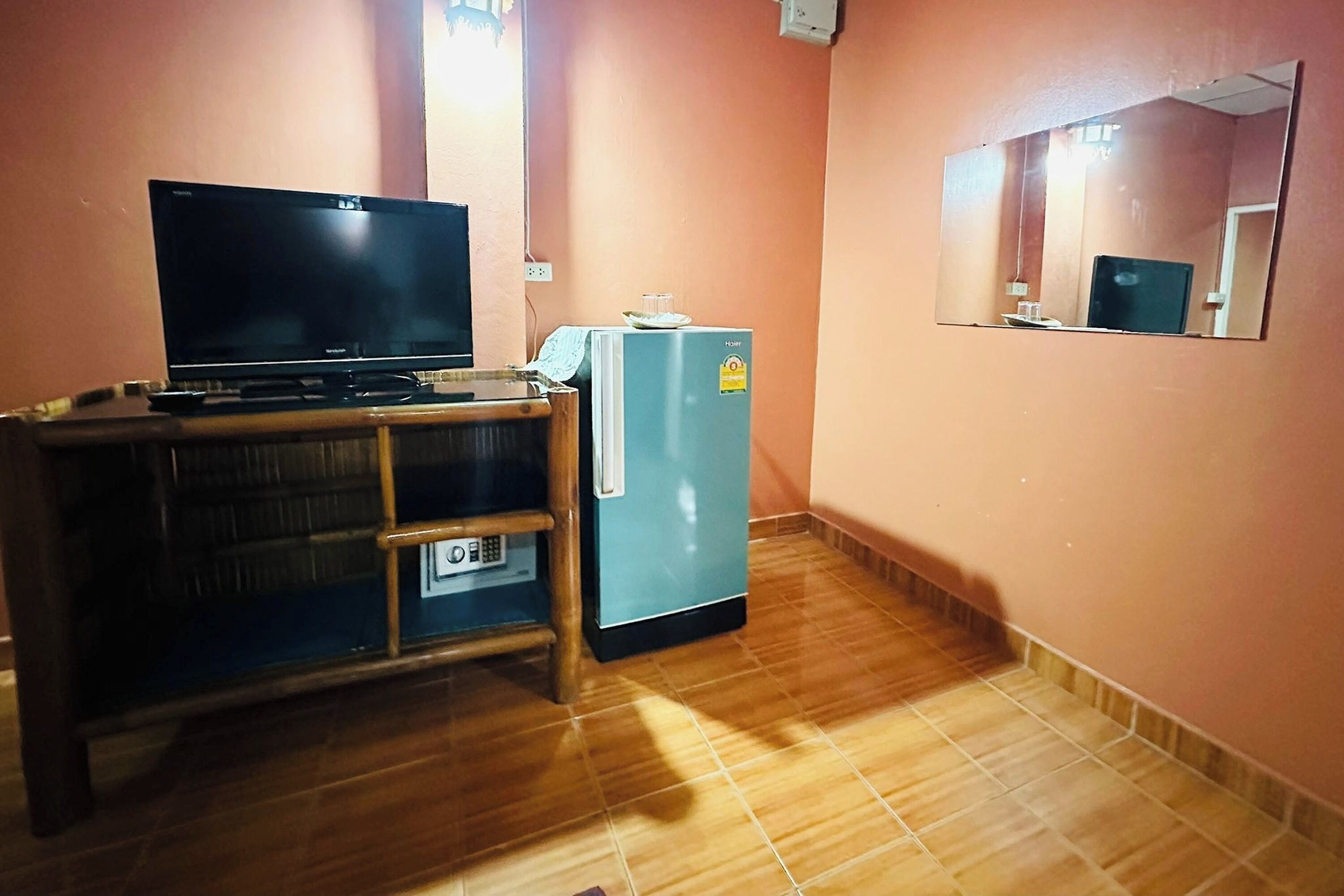 A room with a wooden cabinet, a flat-screen TV, a small refrigerator, and a mirror on the wall.