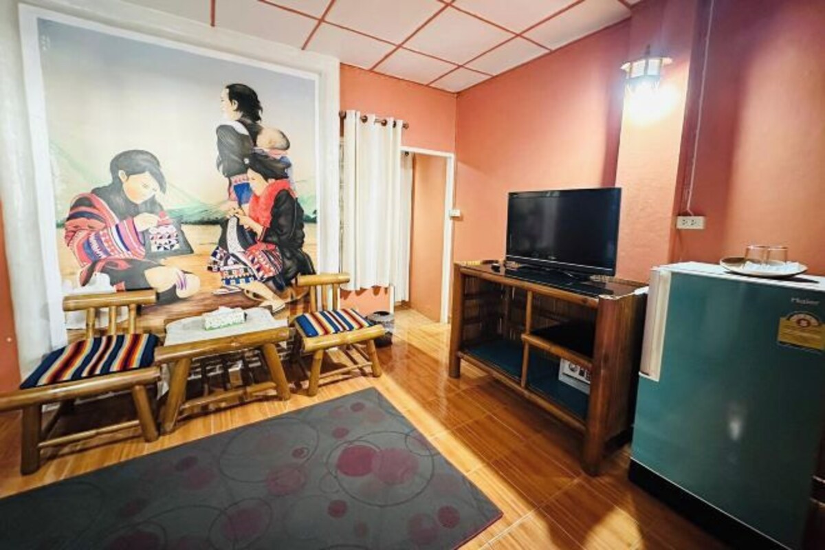 Een woonkamer met een houten vloer, een televisie, een koelkast en een schilderij aan de muur.