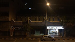 A building with a 'Hello Elvis' sign, a car parked in front, and a streetlight. - Vloft Backpackers Hostel (Ipoh)