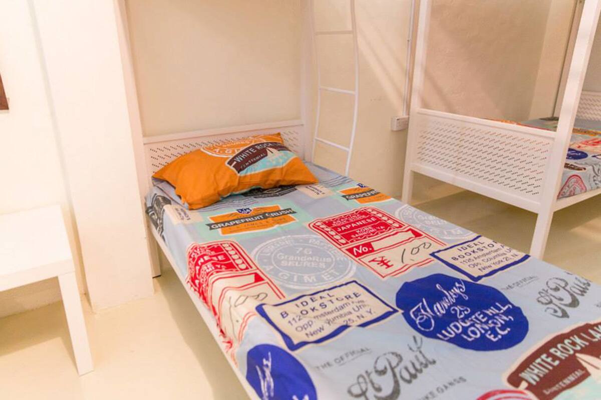 Une chambre avec un lit simple, un cadre de lit en métal blanc, un lit recouvert d’une couvre-lit à motifs et un oreiller.