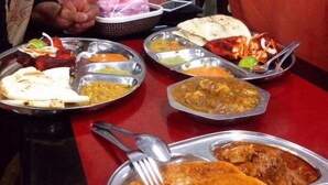A dining table with multiple metal plates of food, including flatbreads, curries, and a meat dish. - Vloft Backpackers Hostel (Ipoh)